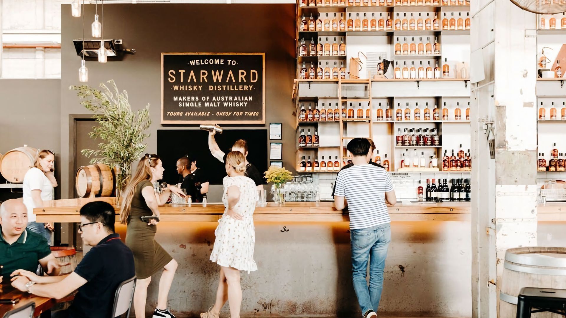 Un espace bar agrémenté d’une enseigne indiquant « Bienvenue à la distillerie de whisky Starward » et de plusieurs étagères remplies de différentes bouteilles.