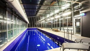 Une piscine intérieure moderne, dotée de parois en verre et d’un banc le long du bord.