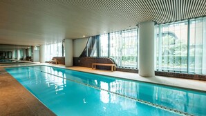 An indoor swimming pool with clear blue water, large windows, and a modern architectural ceiling.