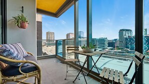 A balcony with wicker furniture, a potted plant, and a view of the cityscape.