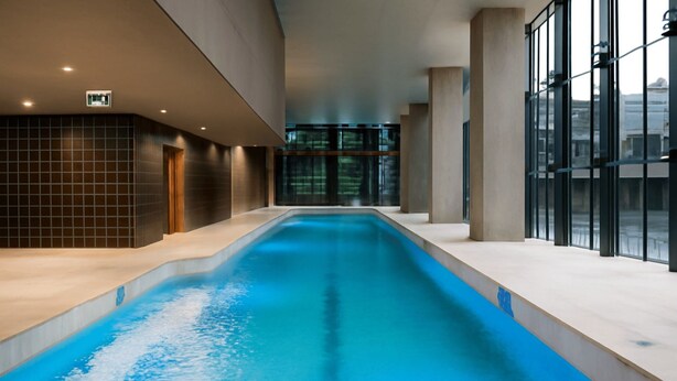 A modern indoor swimming pool with a clear view of the surrounding architecture, including large windows and a tiled wall.