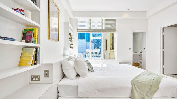 Un dormitorio moderno con una cama grande, paredes blancas y vista a la ciudad desde la ventana.