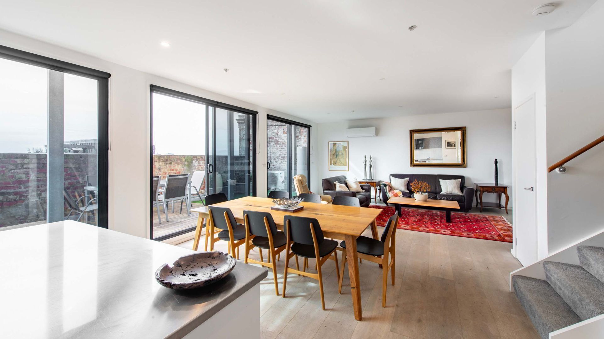 A modern living space with a dining area, a sofa set, and a staircase.