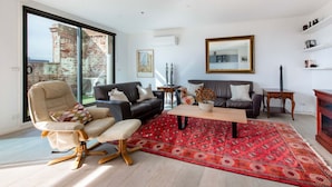 A modern living room with a large window, a red patterned rug, and a mix of leather and fabric furniture. - Sweet Escape - Chocolate Factory (Fitzroy)