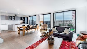 A modern apartment with a kitchen, dining area, and living room. It features large windows, a dining table with chairs, a sofa, and a potted plant. - Sweet Escape - Chocolate Factory (Fitzroy)