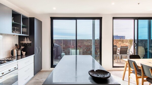 Cuina moderna amb un gran menjador, portes corredisses de vidre que donen a un pati exterior i vista a la ciutat.