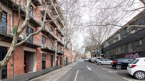 Un carrer amb edificis de maó de diversos pisos, alguns amb balcons i arbres al primer pla.