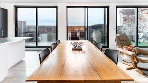A modern dining area with a wooden table, black chairs, and a view through large glass doors to an outdoor space with a brick wall and greenery. - Sweet Escape - Chocolate Factory (Fitzroy)