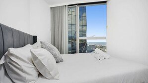 A hotel room with a large bed, a modern headboard, and a view of a cityscape through floor-to-ceiling windows. - Manhattan West Side 57 (Melbourne)