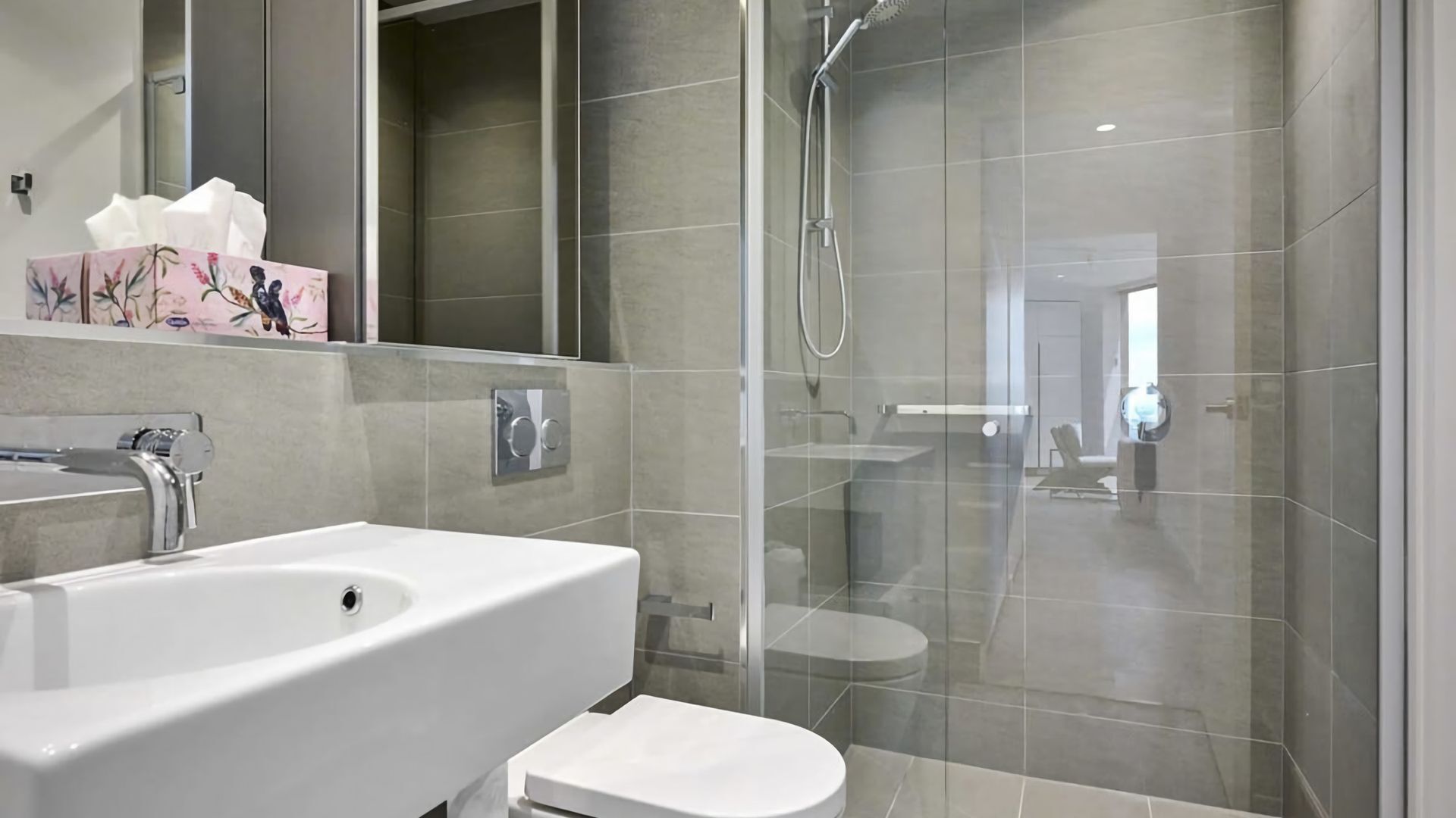 A modern bathroom with a large white sink, a glass shower enclosure, and a toilet.
