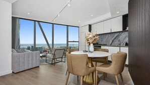 A modern kitchen with a marble backsplash, a dining area with a round table and chairs, and a large window offering a city view. - Manhattan West Side 57 (Melbourne)