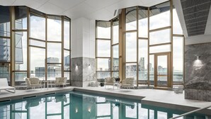 A modern indoor pool area with large windows, seating, and a city view. - Manhattan West Side 57 (Melbourne)