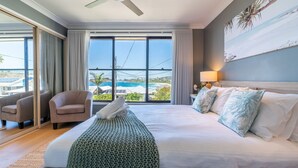 A hotel room with a large bed, a chair, a view of the ocean, and a ceiling fan. - Spectacular Ocean View Home in Bombo (Bombo)