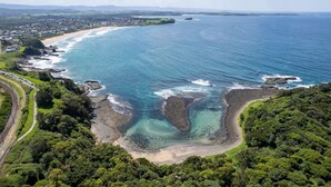 An aerial view of a coastal area with a beach, rocky shoreline, and dense greenery. - Spectacular Ocean View Home in Bombo (Bombo)