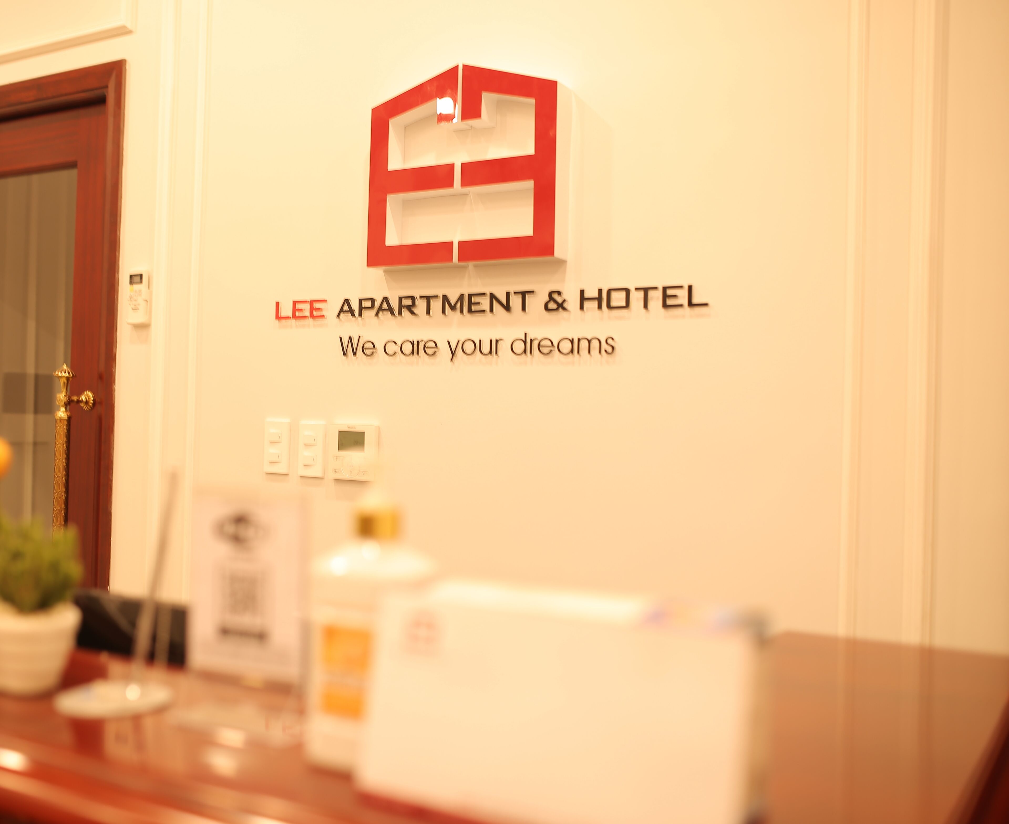 A reception desk with a sign reading "LEE APARTMENT & HOTEL" and a logo above it.