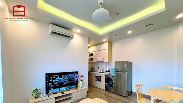 A modern apartment with a flat-screen TV, a washing machine, a refrigerator, and a dining area with a table and chairs. - Lee Apartment & Hotel (Hai Phong)