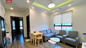 A modern living room with a sofa, two armchairs, a small table, and a TV. - Lee Apartment & Hotel (Hai Phong)