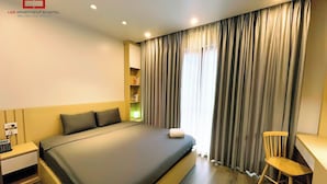 A modern hotel room with a large bed, a desk, and a chair. There is a window with curtains and a shelf with books. - Lee Apartment & Hotel (Hai Phong)