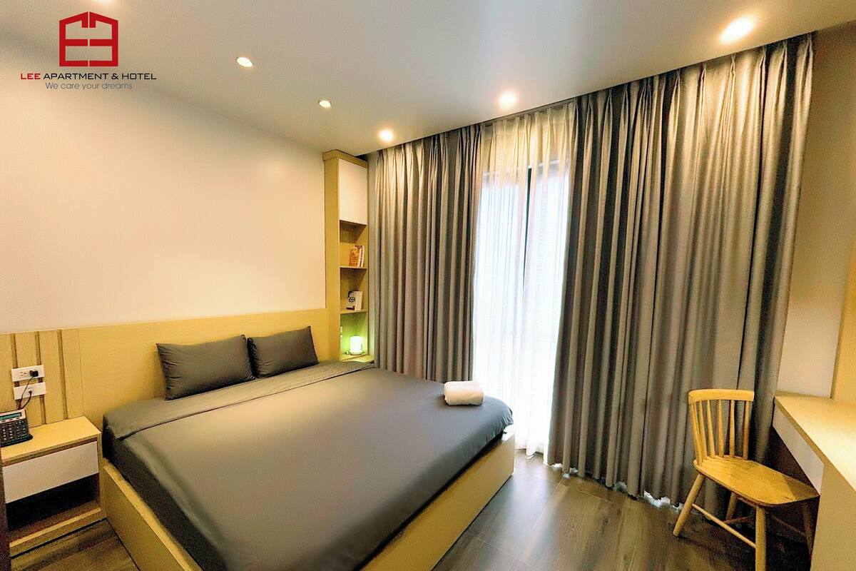 Een moderne hotelkamer met een groot bed, een bureau en een stoel. Er is een raam met gordijnen en een plank met boeken.