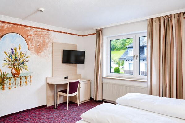 A hotel room with a bed, a desk with a chair, a television, and a window with curtains.