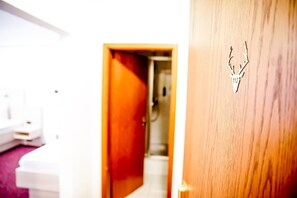 A hotel room with a wooden door, a white wall, and a visible bathroom in the background. - A comfortable and versatile room—perfect for relaxing, working, and socializing (Winterberg)