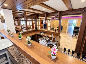 A hotel lobby with a wooden reception desk, potted orchids, a coffee machine, and a seating area with a view of the outdoor space. - A comfortable and versatile room—perfect for relaxation, work, and socializing (Winterberg)
