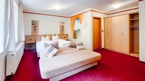 Een kamer met een bed, een kledingkast, een spiegel en een roodgekleurd tapijt.