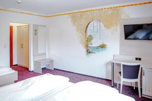 A hotel room with a bed, a desk, a chair, a TV, and a wall with a decorative painting. - A comfortable and versatile room—perfect for relaxation, work, and socializing (Winterberg)