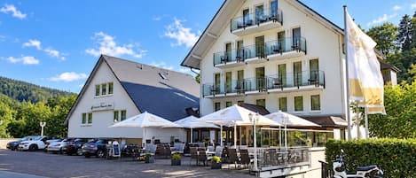 A hotel with outdoor seating, a parking area, and a flag.