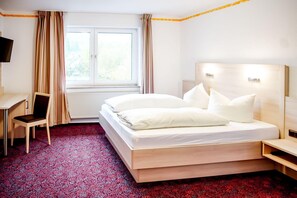 A hotel room with a bed, a desk, a chair, a TV, and a window with curtains. - A comfortable and versatile room—perfect for relaxation, work, and socializing (Winterberg)