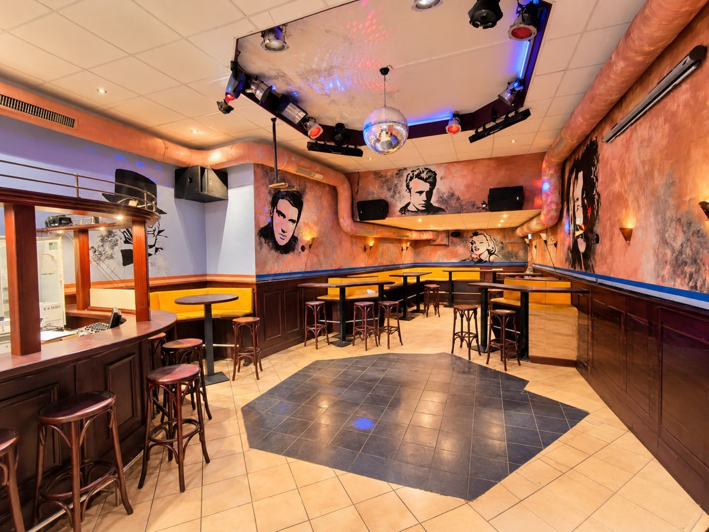 A bar area with multiple stools, a stage with lighting equipment, and wall art.