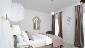 Quarto com cama, mesa de cabeceira, abajur e janela com cortinas.
