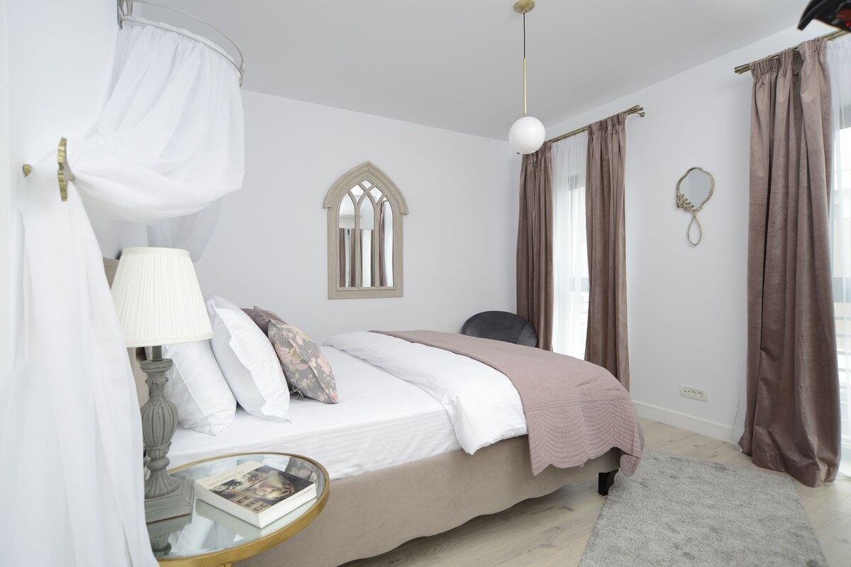 A bedroom with a bed, bedside table, lamp, and a window with curtains.
