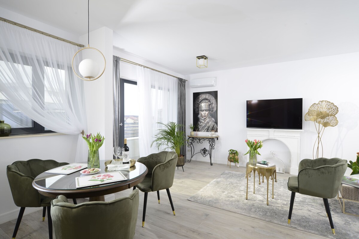 Una sala de estar moderna con una mesa redonda de vidrio, sillas tapizadas en verde, un televisor de pantalla plana montado en la pared y una chimenea.