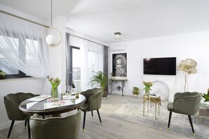 Una sala de estar moderna con una mesa redonda de vidrio, sillas tapizadas en verde, un televisor de pantalla plana montado en la pared y una chimenea.