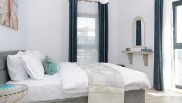Un dormitorio moderno con cama gris, ropa de cama blanca, un cojín turquesa, una mesita de cristal, una lámpara dorada y un cartel con la palabra 'relax'.