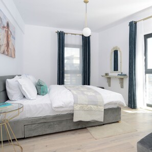 Un dormitorio moderno con cama gris, ropa de cama blanca, un cojín turquesa, una mesita de cristal, una lámpara dorada y un cartel con la palabra 'relax'.