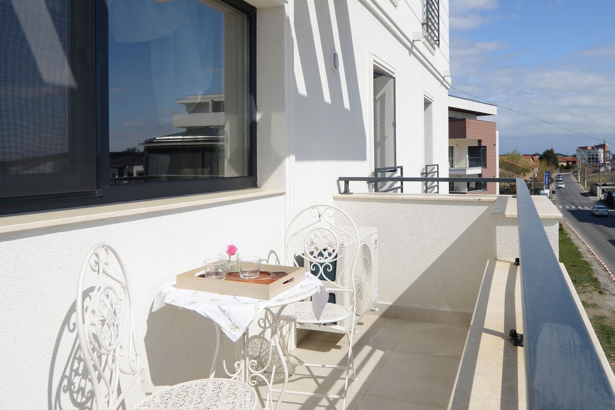 Un balcon avec une table et des chaises, une fenêtre et une vue sur la rue.
