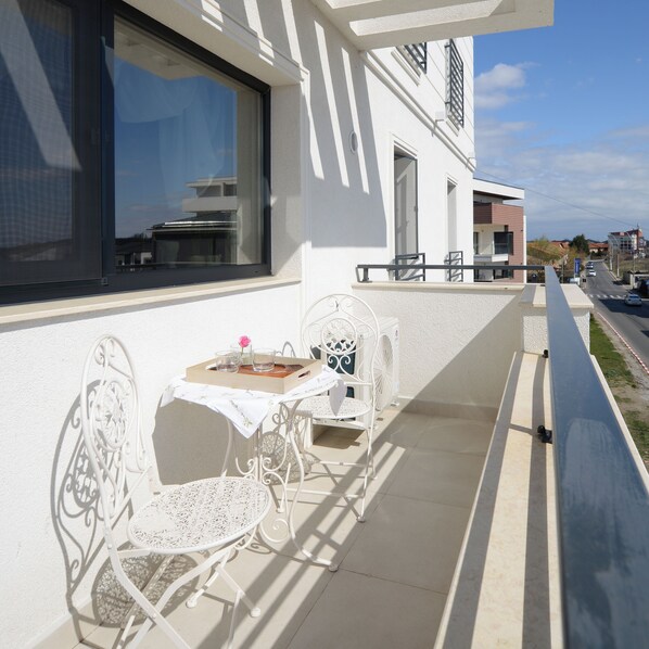 Un balcon avec une table et des chaises, une fenêtre et une vue sur la rue.