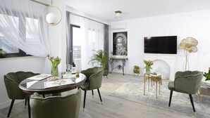 Ein modernes Wohnzimmer mit einem runden Glastisch, grünen Polstersesseln, einem flachbildfernseher an der Wand und einem Kamin.