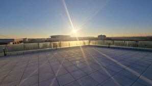 Eine Dachterrasse mit freiem Blick auf den Sonnenuntergang, mit Fliesenböden und einem Metallgeländer.