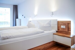 Quarto de hotel moderno com uma cama grande, mesas de cabeceira, uma parede de destaque em madeira e uma janela com cortinas.