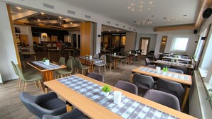 A modern dining area with multiple tables and chairs, a kitchen in the background, and a view of the outdoors. - Comfortable and versatile room -perfect for relaxation, work and exchange (Winterberg)