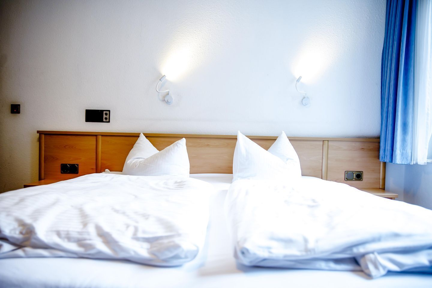 A hotel room with a wooden headboard, two bedside tables, a bed with white linens, and two wall-mounted light fixtures.