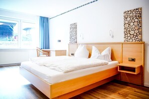 A modern hotel room with a wooden bed, bedside tables, a desk, and a view of the outdoors. - A comfortable and versatile room—perfect for relaxation, work, and socializing (Winterberg)