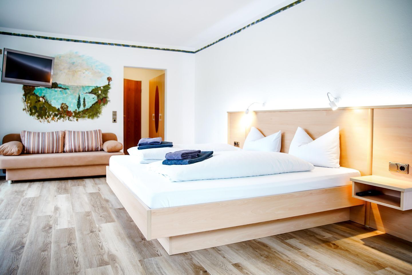 A modern hotel room with a bed, bedside table, and a television mounted on the wall.
