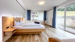 A modern bedroom with a large bed, a bedside table, a nightstand, a window with curtains, and a view of the outdoors. - Comfortable and versatile room -perfect for relaxation, work and exchange (Winterberg)