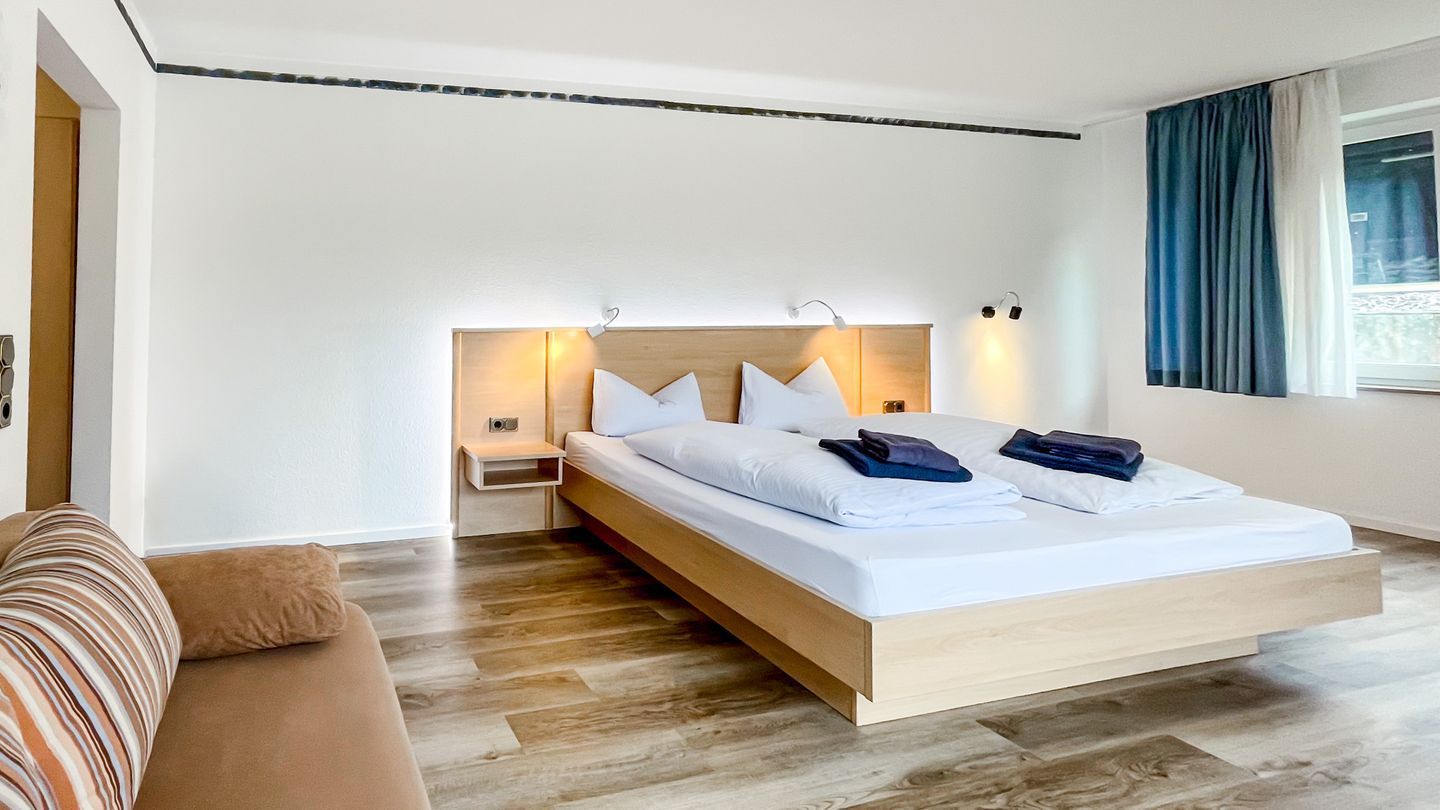 A modern bedroom with a wooden bed, white linens, and a nightstand with a lamp.
