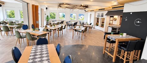 A modern dining area with multiple tables and chairs, large windows, and a central decorative element.