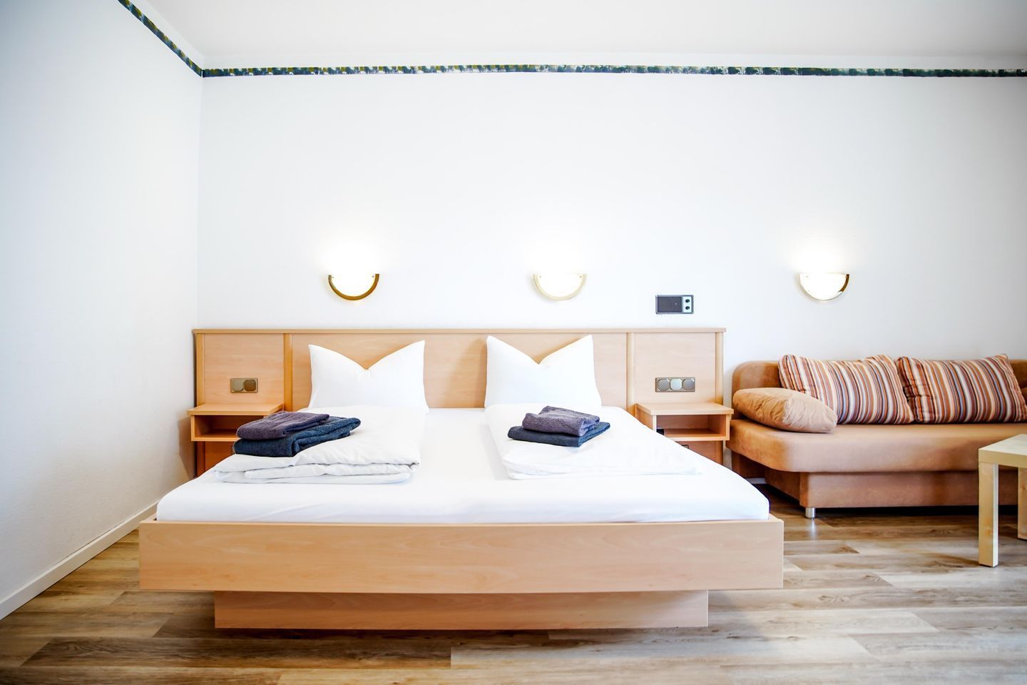 Un dormitorio moderno con una cama grande, mesitas de noche, un pouf y luces fijadas en la pared.